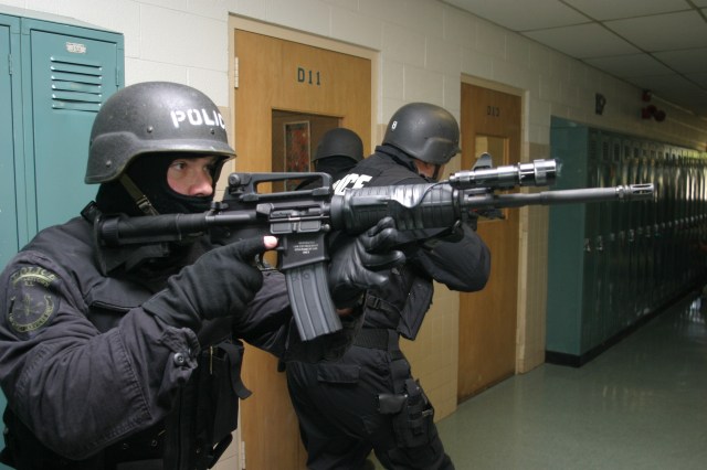 Police in a school hallway with rifles drawn and in SWAT gear